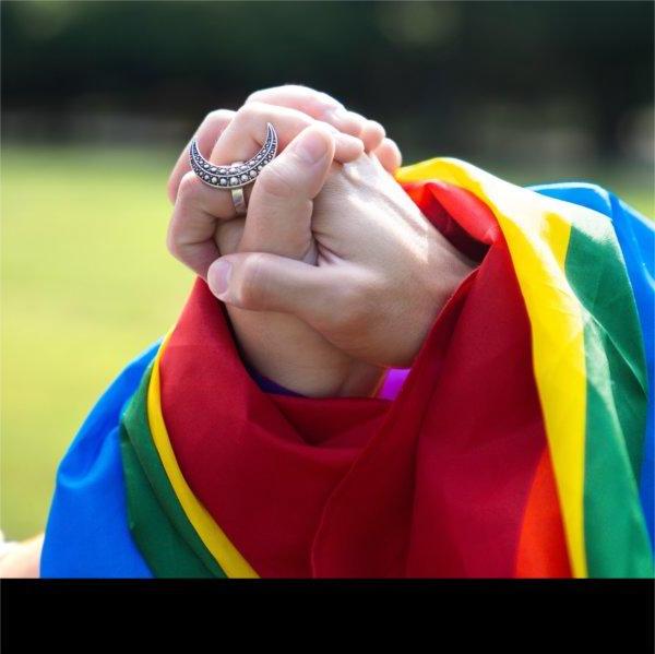 Two folded hands draped with a rainbow pride flag.