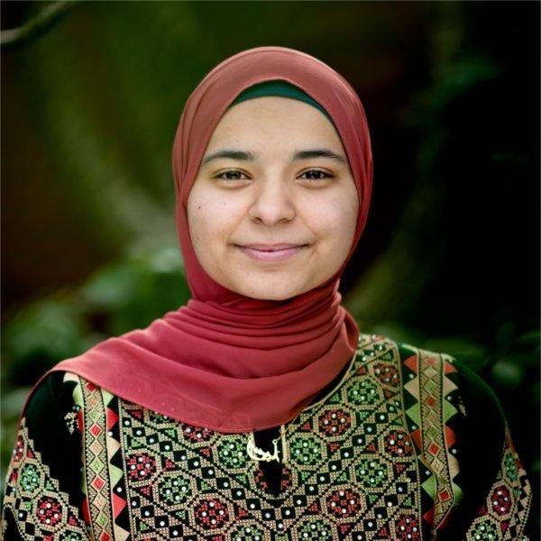 Aseel Ayesh standing outside in a maroon hajib