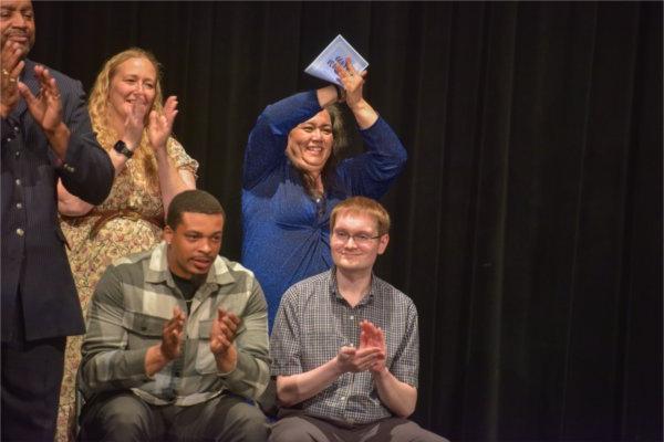 people in back row standing to clap, two people seated in front also clapping